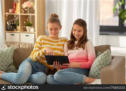 people, technology and friendship concept - happy teenage girls with tablet pc computer sitting on sofa at home. happy girls with tablet pc sitting on sofa at home