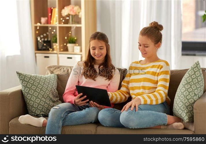 people, technology and friendship concept - happy teenage girls with tablet pc computer sitting on sofa at home. happy girls with tablet pc sitting on sofa at home