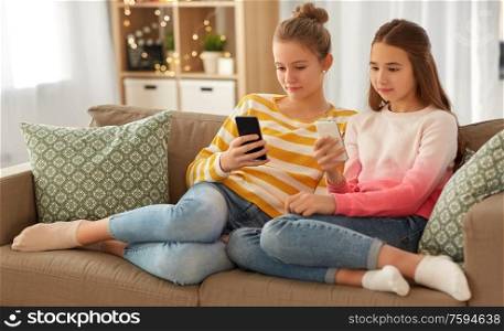 people, technology and friendship concept - teenage girls with smartphones sitting on sofa at home. girls with smartphones sitting on sofa at home