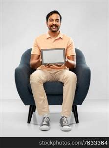 people, technology and furniture concept - happy smiling young indian with tablet pc computer man sitting in chair over grey background. happy indian man with tablet pc computer in chair