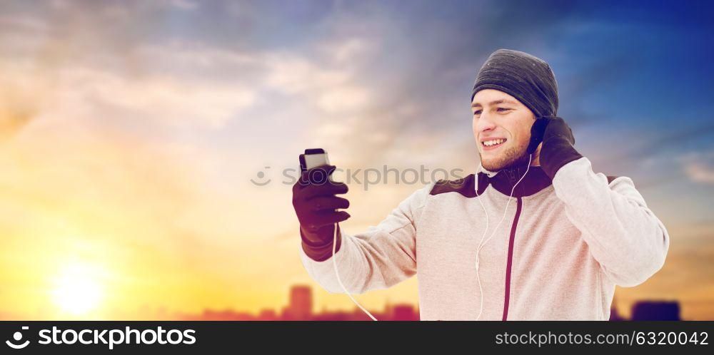 people, technology and healthy lifestyle concept - happy smiling young man in earphones with smartphone listening to music outdoors. happy man with earphones and smartphone in winter