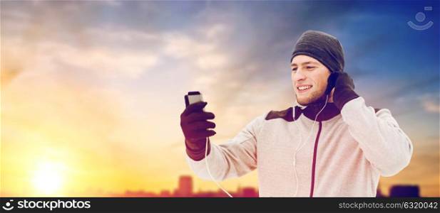 people, technology and healthy lifestyle concept - happy smiling young man in earphones with smartphone listening to music outdoors. happy man with earphones and smartphone in winter