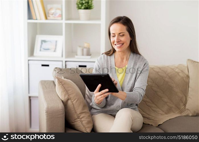 people, technology and internet concept - happy woman sitting on sofa with tablet pc computer at home. happy woman with tablet pc at home