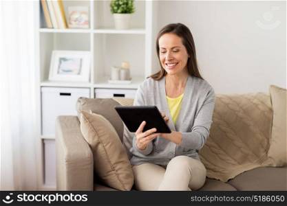 people, technology and internet concept - happy woman sitting on sofa with tablet pc computer at home. happy woman with tablet pc at home