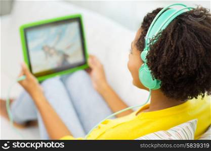 people, technology and leisure concept - close up of happy african american young woman lying with tablet pc computer and headphones listening to music and watching video at home