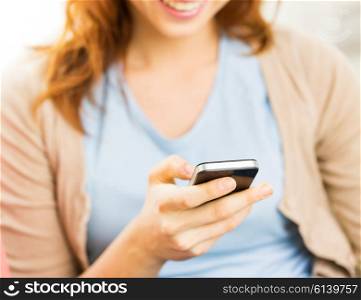 people, technology and leisure concept - close up of young woman texting on smartphone at home