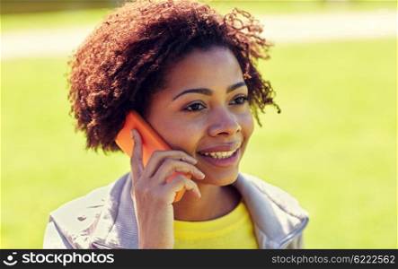 people, technology and leisure concept - happy african american young woman calling on smartphone outdoors
