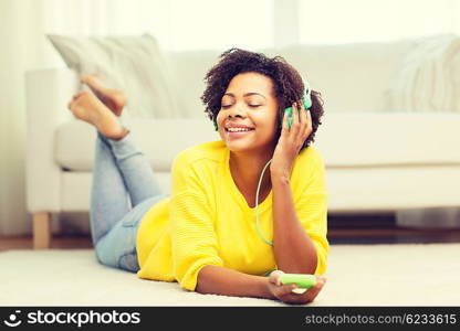 people, technology and leisure concept - happy african american young woman lying on floor with smartphone and headphones listening to music at home