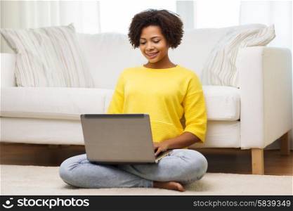 people, technology and leisure concept - happy african american young woman sitting on floor with laptop computer at home