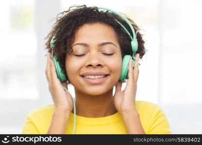 people, technology and leisure concept - happy african american young woman sitting on sofa with headphones listening to music at home