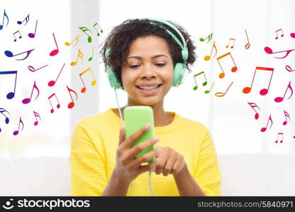 people, technology and leisure concept - happy african american young woman sitting on sofa with smartphone and headphones listening to music at home over notes background