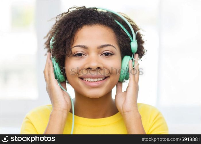 people, technology and leisure concept - happy african american young woman sitting on sofa with headphones listening to music at home