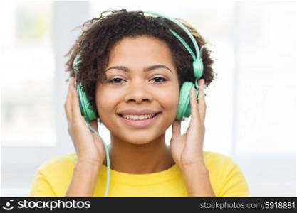 people, technology and leisure concept - happy african american young woman sitting on sofa with headphones listening to music at home
