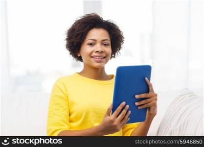 people, technology and leisure concept - happy african american young woman sitting on sofa with tablet pc computer at home