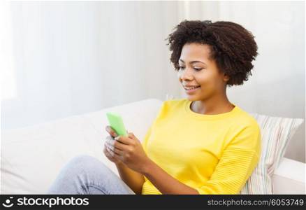 people, technology and leisure concept - happy african american young woman sitting on sofa with smartphone at home