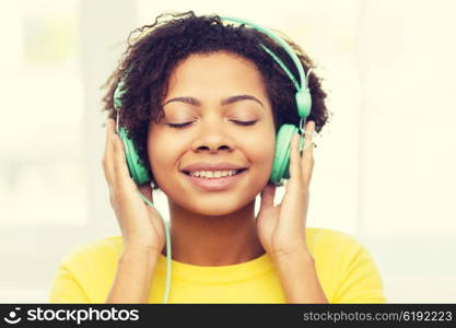 people, technology and leisure concept - happy african american young woman sitting on sofa with headphones listening to music at home