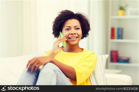 people, technology and leisure concept - happy african american young woman sitting on sofa with smartphone at home