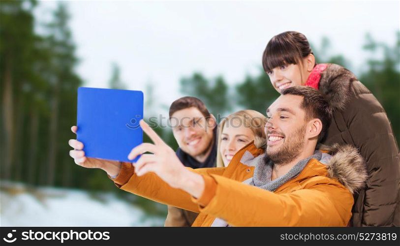 people, technology and leisure concept - happy friends taking selfie with tablet pc computer over winter outdoor background. friends with tablet pc taking selfie in winter