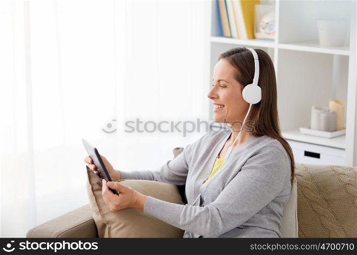people, technology and leisure concept - happy middle-aged woman sitting on sofa with tablet pc computer and headphones listening to music at home. happy woman with tablet pc and headphones at home. happy woman with tablet pc and headphones at home
