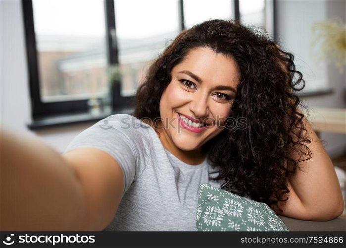 people, technology and leisure concept - happy smiling young woman taking selfie at home. happy smiling young woman taking selfie at home