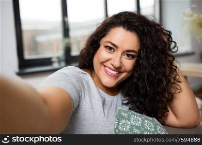 people, technology and leisure concept - happy smiling young woman taking selfie at home. happy smiling young woman taking selfie at home