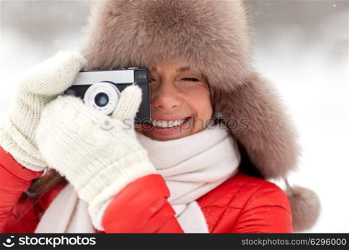 people, technology and leisure concept - happy woman in winter fur hat taking picture by film camera outdoors. happy woman with film camera outdoors in winter