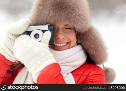 people, technology and leisure concept - happy woman in winter fur hat taking picture by film camera outdoors. happy woman with film camera outdoors in winter