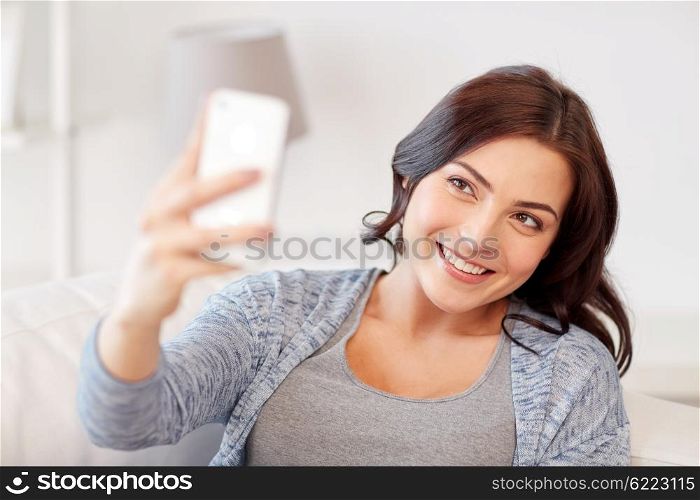 people, technology and leisure concept - happy woman taking selfie with smartphone at home