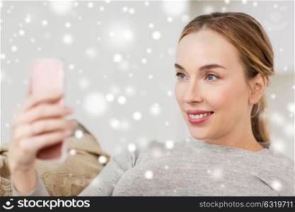 people, technology and leisure concept - happy woman taking selfie with smartphone at home over snow. happy woman taking selfie with smartphone at home