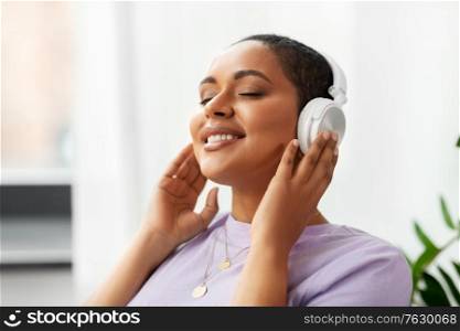 people, technology and leisure concept - happy young african american woman in headphones listening to music at home. woman in headphones listening to music at home