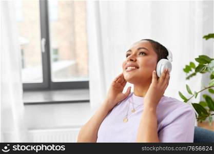 people, technology and leisure concept - happy young african american woman in headphones listening to music at home. woman in headphones listening to music at home