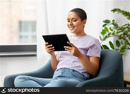 people, technology and leisure concept - happy young african american woman with tablet pc computer sitting in chair at home. african american woman with tablet pc at home