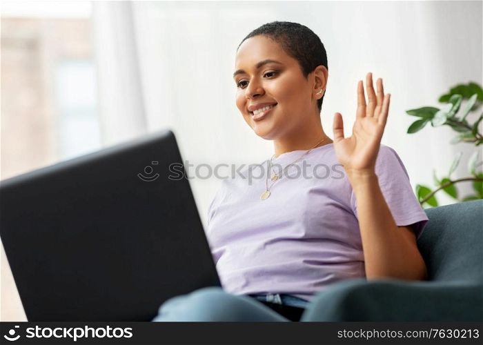 people, technology and leisure concept - happy young african american woman with laptop computer having video call at home. african woman with laptop having video call