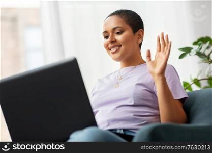 people, technology and leisure concept - happy young african american woman with laptop computer having video call at home. african woman with laptop having video call