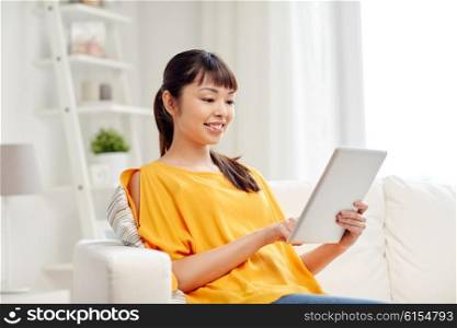 people, technology and leisure concept - happy young asian woman sitting on sofa with tablet pc computer at home