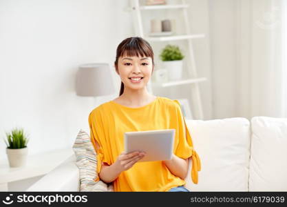 people, technology and leisure concept - happy young asian woman sitting on sofa with tablet pc computer at home