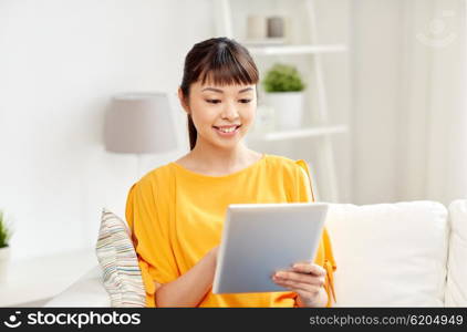 people, technology and leisure concept - happy young asian woman sitting on sofa with tablet pc computer at home