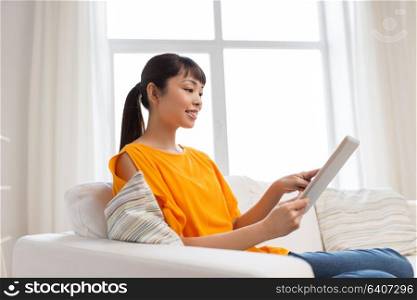 people, technology and leisure concept - happy young asian woman sitting on sofa with tablet pc computer at home. happy young asian woman with tablet pc at home