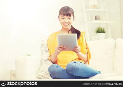 people, technology and leisure concept - happy young asian woman sitting on sofa with tablet pc computer at home. happy young asian woman with tablet pc at home. happy young asian woman with tablet pc at home
