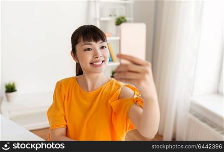 people, technology and leisure concept - happy young asian woman taking selfie by smartphone at home. happy asian woman taking selfie by smartphone