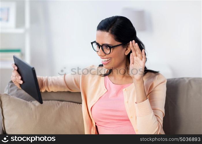 people, technology and leisure concept - happy young indian woman sitting on sofa with tablet pc computer and having video call at home. woman with tablet pc having video call at home