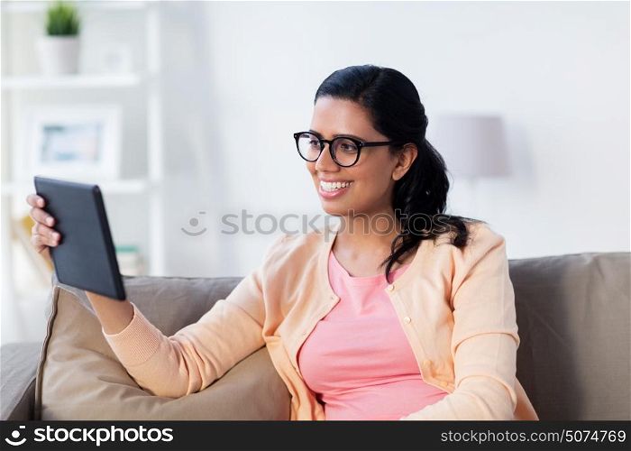 people, technology and leisure concept - happy young indian woman sitting on sofa with tablet pc computer at home. happy indian woman with tablet pc at home