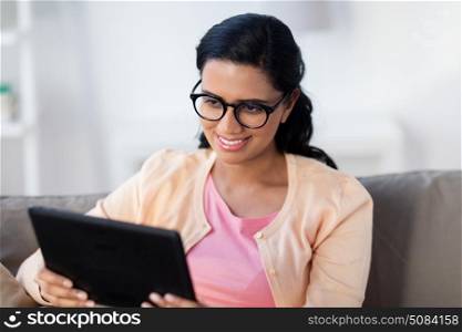people, technology and leisure concept - happy young indian woman sitting on sofa with tablet pc computer at home. happy indian woman with tablet pc at home. happy indian woman with tablet pc at home