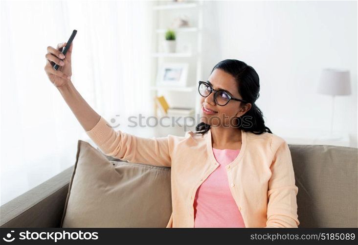 people, technology and leisure concept - happy young indian woman taking selfie on smartphone at home. happy woman taking selfie with smartphone at home