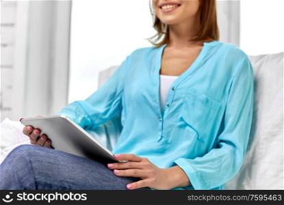 people, technology and leisure concept - happy young woman sitting on sofa with tablet pc computer at home. happy woman with tablet pc at home