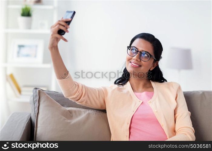 people, technology and leisure concept - happy young woman taking selfie on smartphone at home. happy woman taking selfie with smartphone at home