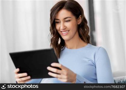 people, technology and leisure concept - happy young woman with tablet pc computer sitting in chair at home. happy smiling young woman with tablet pc at home
