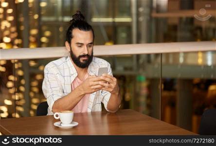 people, technology and leisure concept - man drinking coffee and messaging on smartphone at restaurant or cafe. man with coffee and smartphone at restaurant