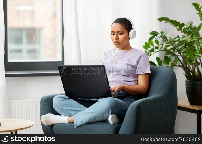 people, technology and leisure concept - young african american woman in headphones with laptop computer listening to music at home. woman with laptop listening to music at home