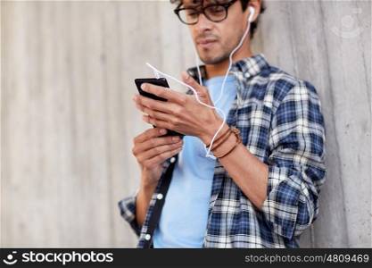 people, technology and lifestyle - close up of young hipster man with earphones and smartphone listening to music